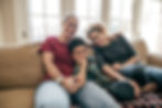 A family of three people sitting on a couch with arms around each other