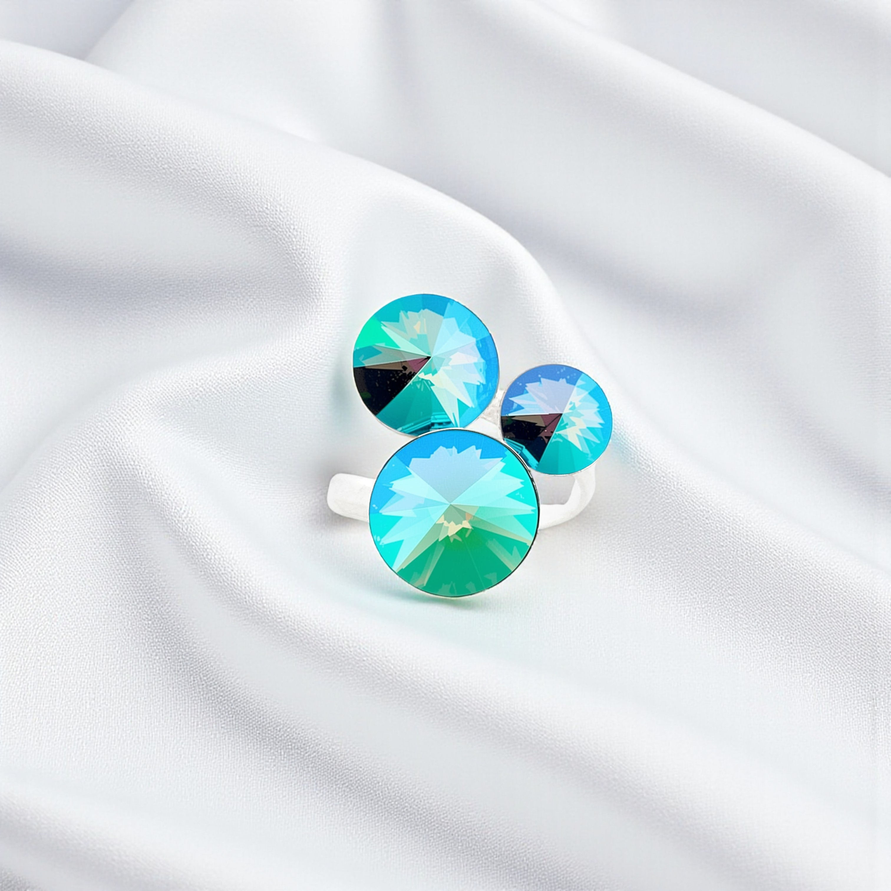 Bague scintillante en argent 925 avec trois pierres Swarovski Paradise Shine posée sur un tissu satiné blanc.
