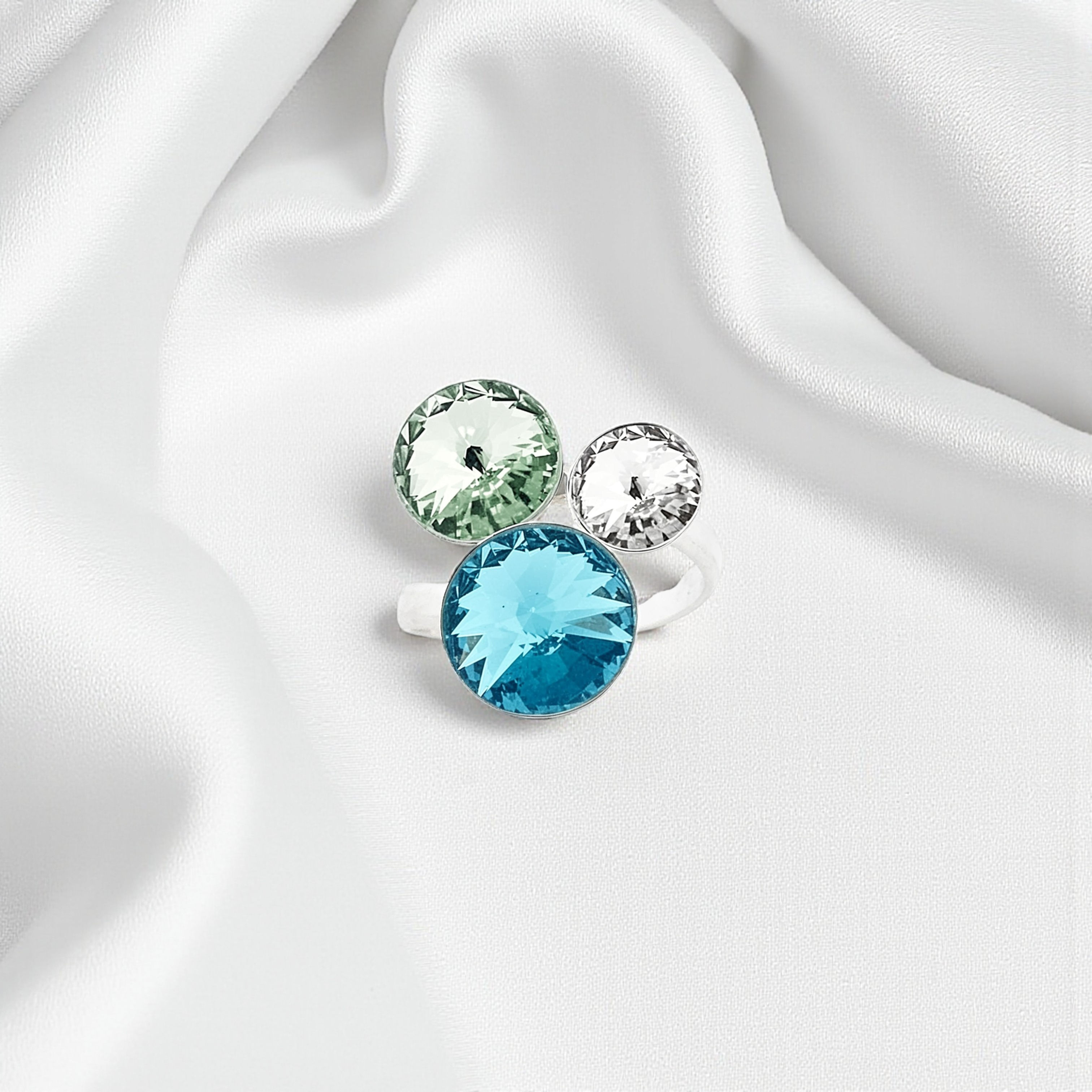 Bague en argent 925 à trois pierres Swarovski posée sur un tissu satiné blanc, éclairage doux mettant en valeur les reflets.