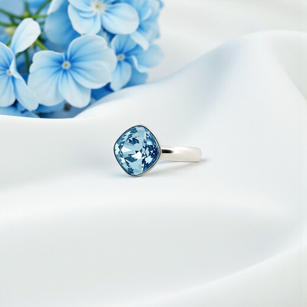 Bague en argent 925 ornée d’un cristal Swarovski® bleu aquamarine de 10 mm, posée sur tissu blanc avec fleurs bleues.