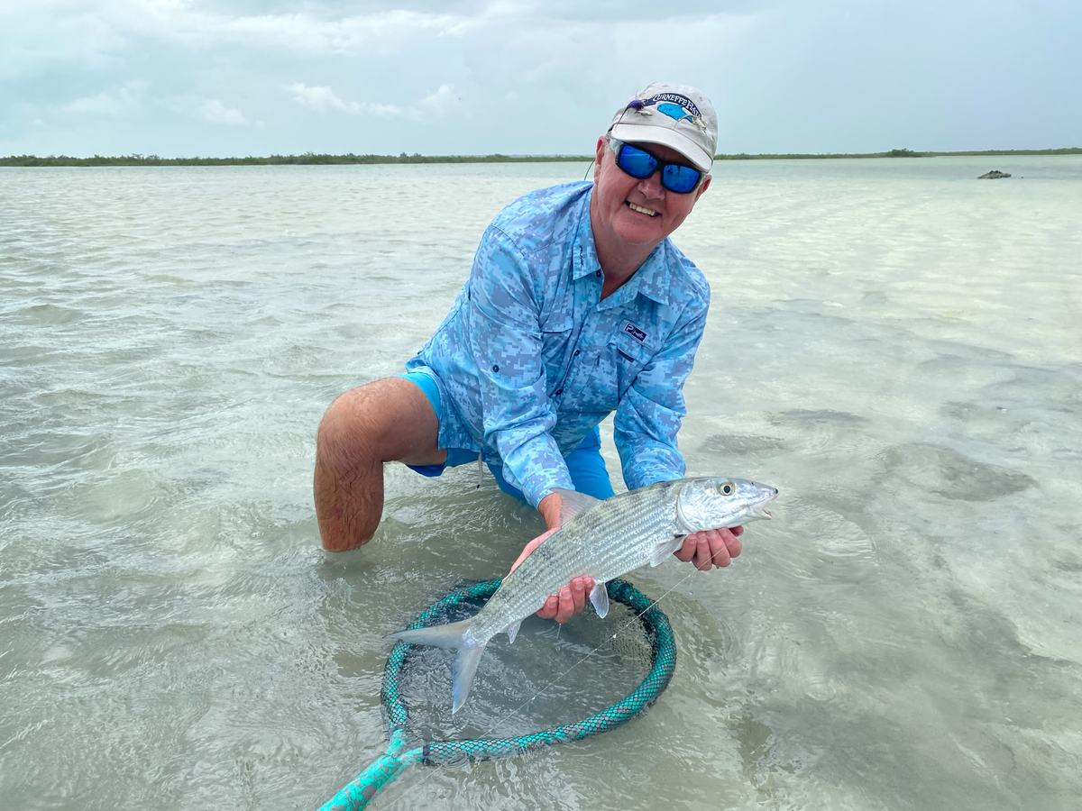 Angler kneeling with a bonefish on a shallow flat