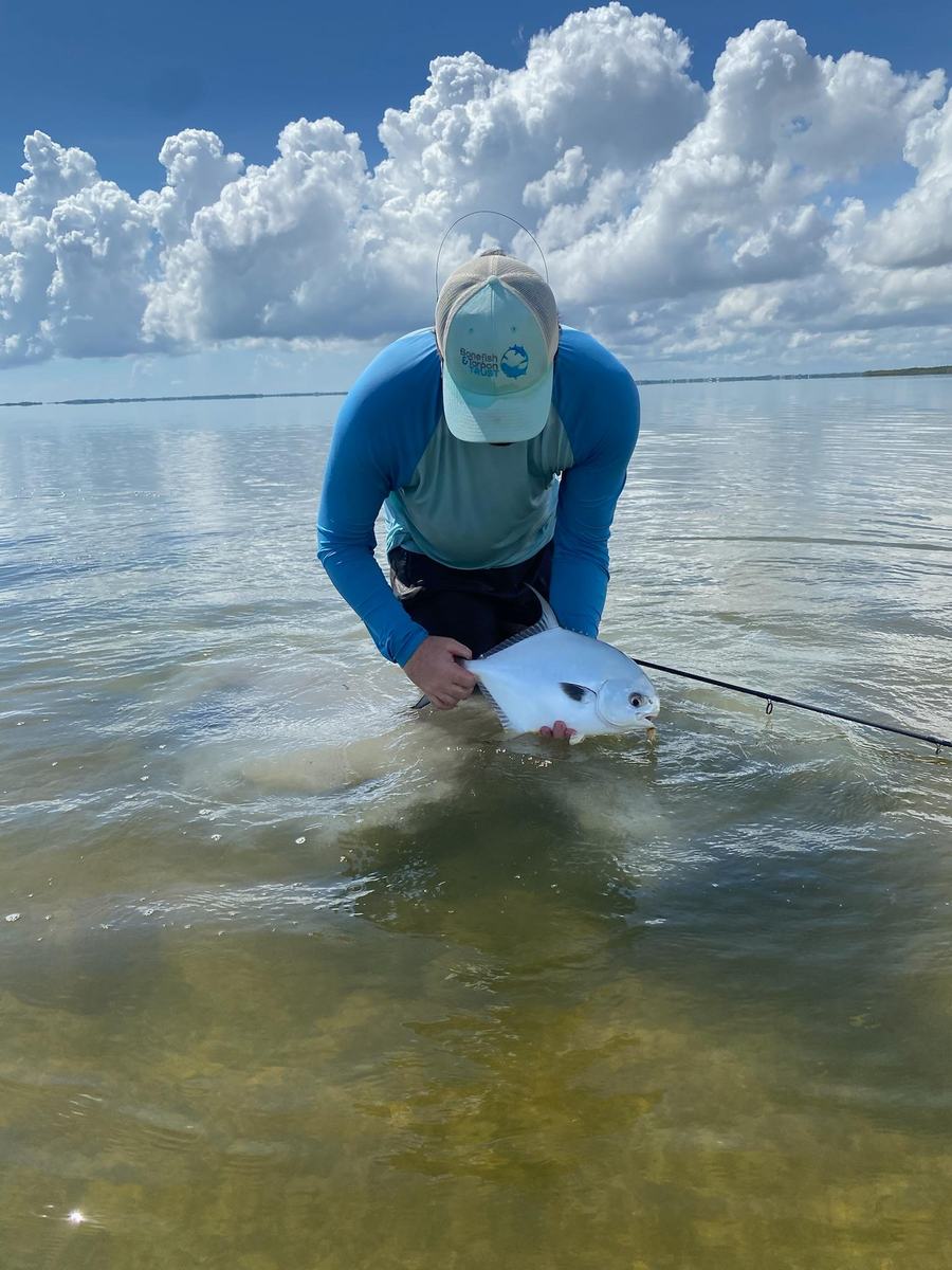 Angler releasing a permit under big clouds