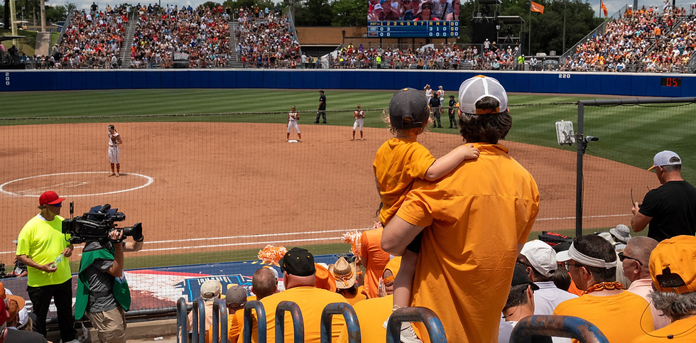 SOFTBALL FAN CARRYING CHILD WATCHING SOFTBALL GAME