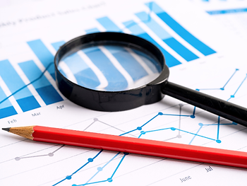 Magnifying glass and red pencil on blue bar and line charts with month labels, suggesting data analysis and review.