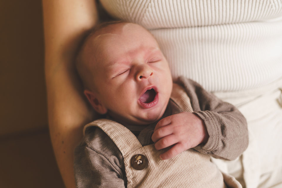 Newborn baby ligt in armen van moeder en gaapt tijdens een newborn fotoshoot in Den Haag