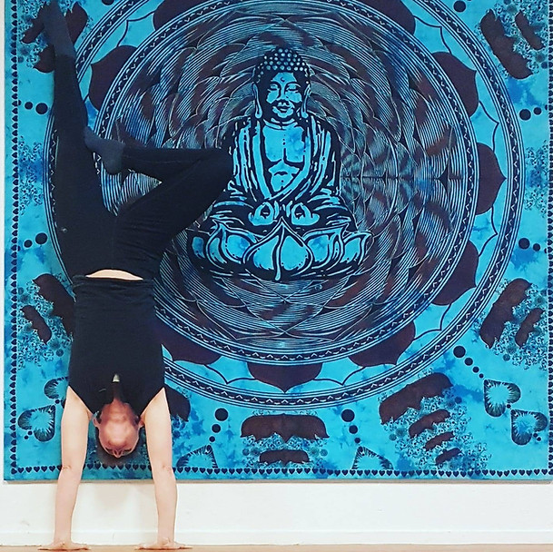 Een vrouw doet yoga een handstan met en boedha op de achtergrond.