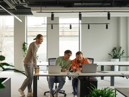 Three startup team members review a phone and laptops together at a shared desk in an open-plan office, an example of high-agency startup talent working across functions.