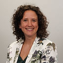 Headshot of Mairi Gougeon, who has shoulder length curly hair, a big smile and a floral jacket on