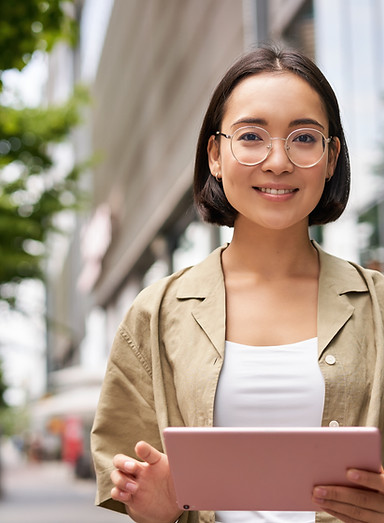 outdoor-shot-young-korean-woman-stands-street-with-laptop-wears-glasses-reads-smiles-happi