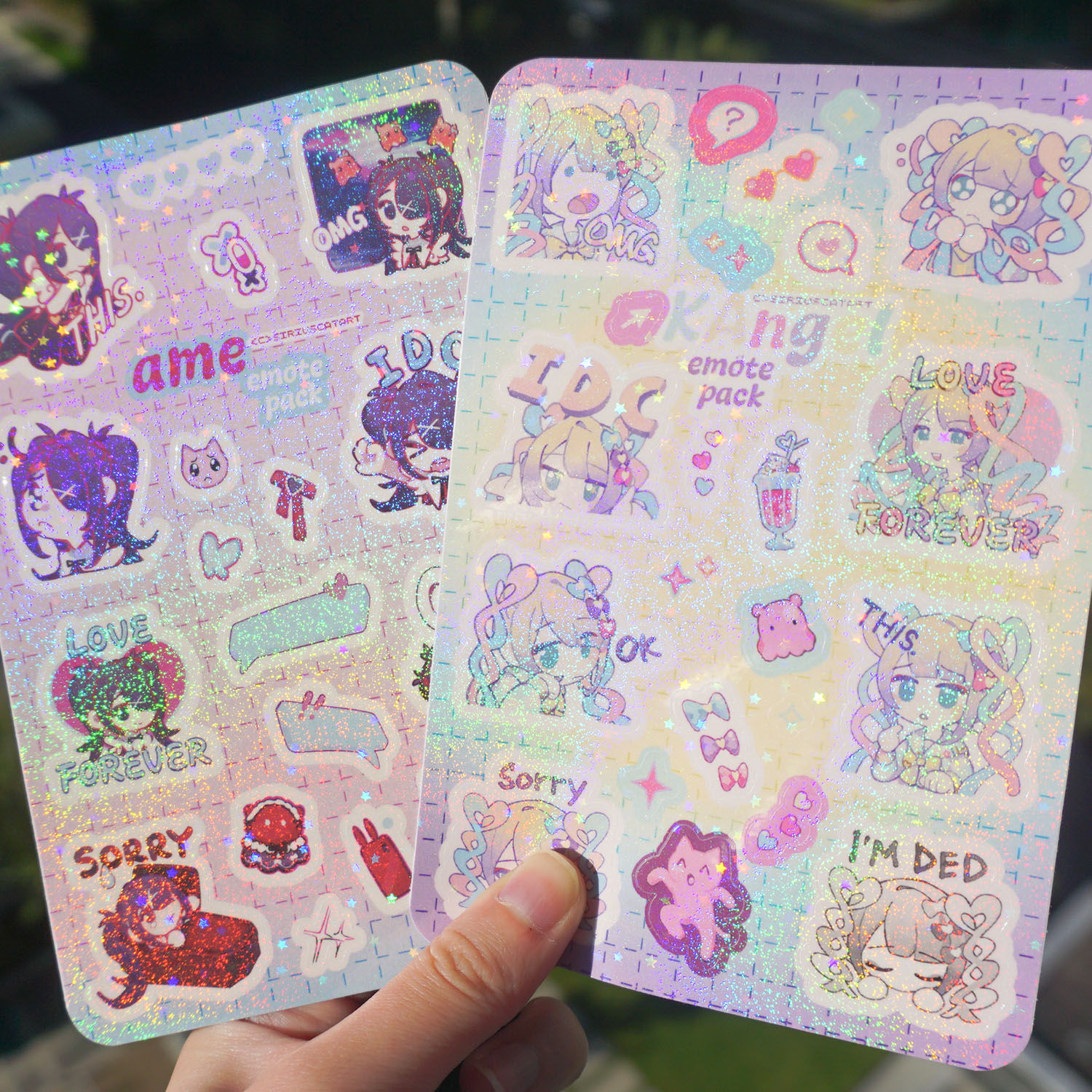 Two Needy Streamer Overload glitter sticker sheets merch each with 8 KAngel and Ame emote stickers glowing under the sun