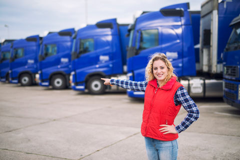 female-trucker-standing-in-front-of-parked-trucks-and-pointing-her-finger-to-the-transport