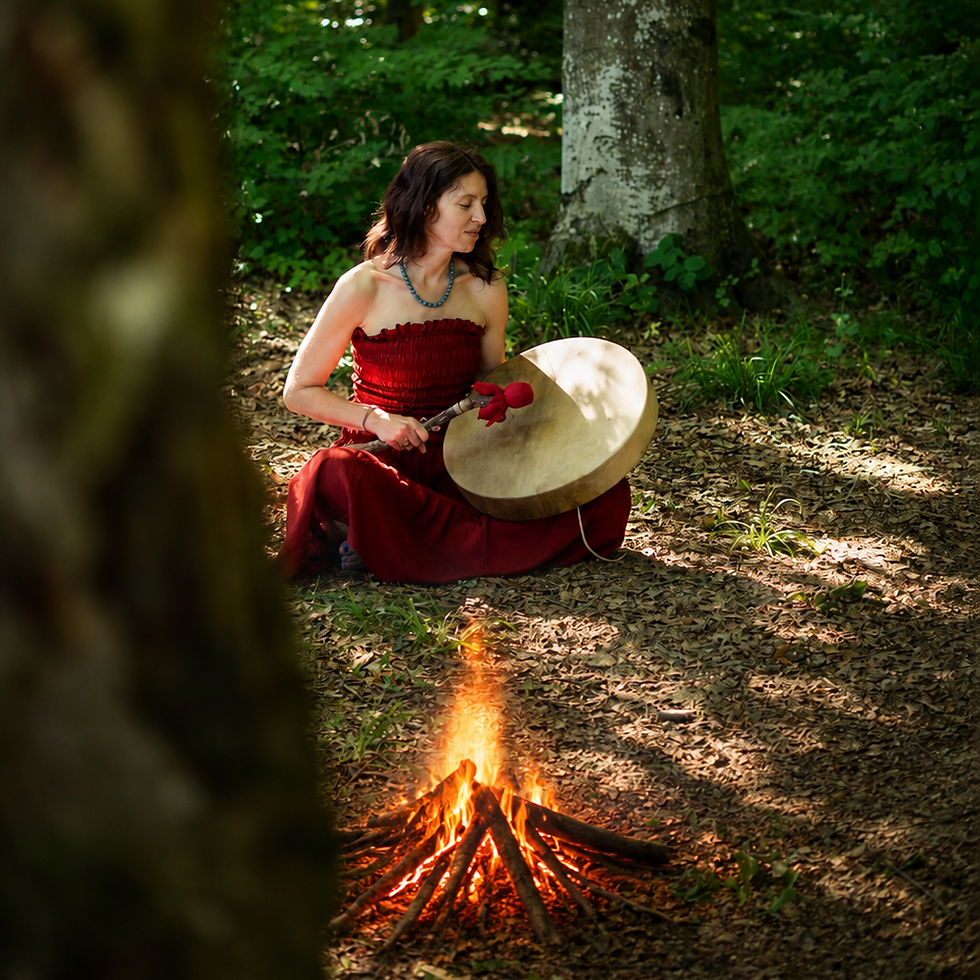 Frau in einem roten Kleid, die sitzend im Wald auf einer Trommel spielt. Davor brennt ein Lagerfeuer.