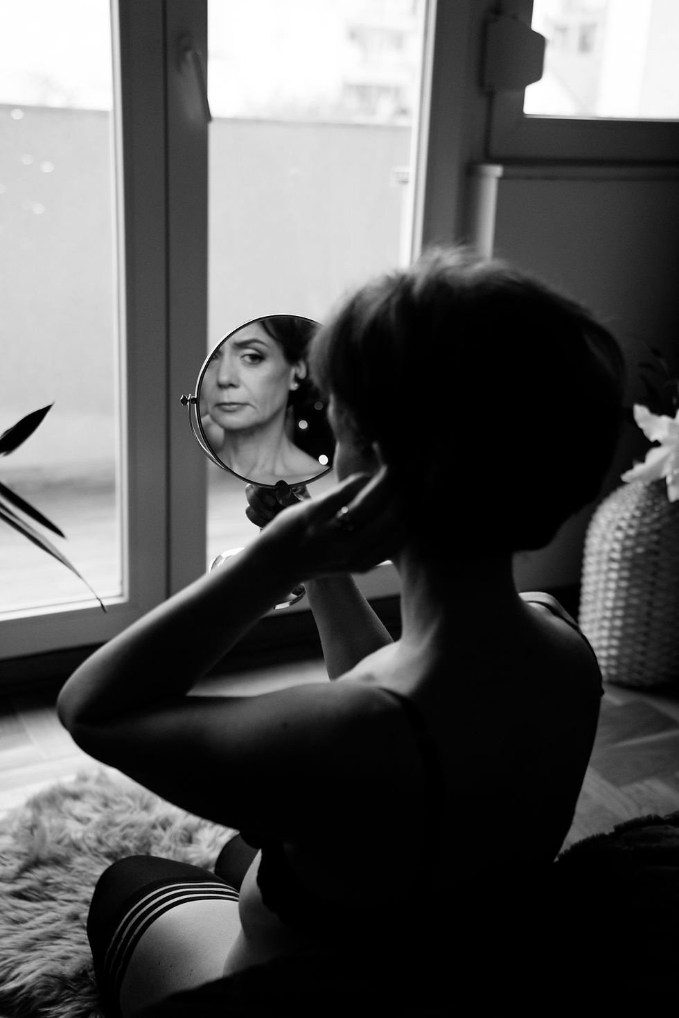 Žena posmatra svoj odraz u ogledalu tokom boudoir fotografisanja