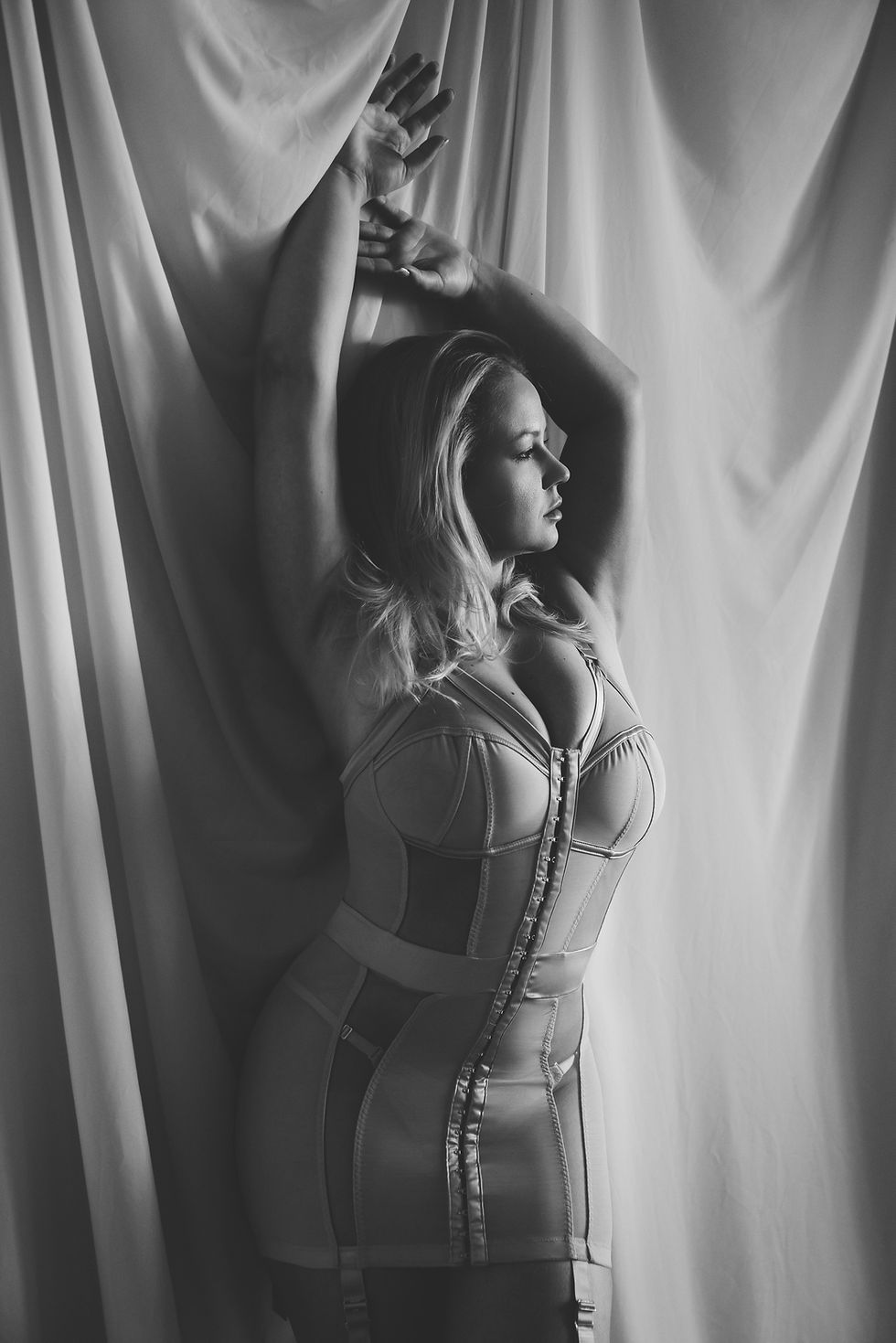 Žena u korsetu tokom boudoir fotografisanja pored prozora