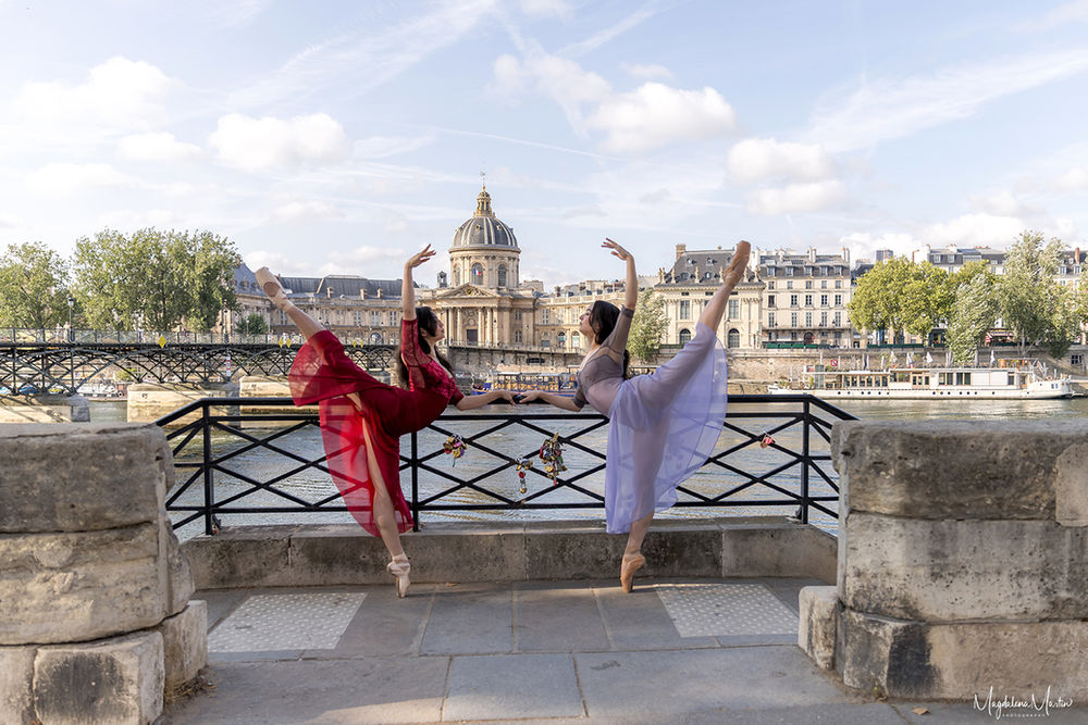 Twin ballerinas dancing together along the Seine with the Institut de France in the background in Paris.
