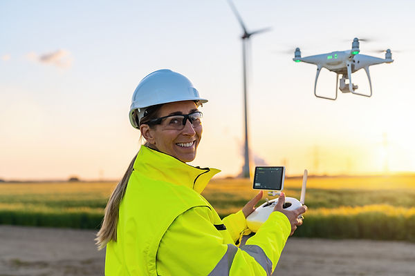 Happy Female Operator inspecting Wind turbine with drone at sunset. Drone inspection conce