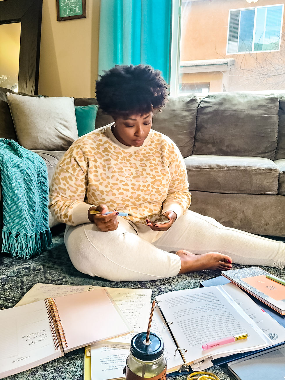 African American woman sitting on floor, surrounded by journals and planners. Planning and strategy help optimize business. Shanell Tyus. Curly hair. Taper cut. Leopard print. Cozy at home. Cozy home shot. Planning and strategizing.