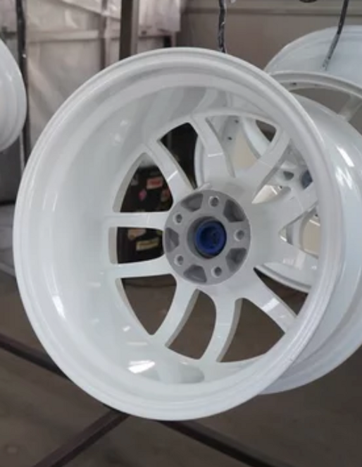 Matte white alloy wheel hanging to cure, showcasing Rhino Coatings’ durable and standout finishes for car enthusiasts and restorers.
