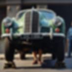 Classic green car raised on stands with legs visible beneath, representing Foxhills Body Shop’s support for local car enthusiasts through prep work, paint, and restoration advice.