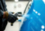Close-up of a spray gun applying blue paint to a car panel, representing Foxhills’ cosmetic car resprays and panel upgrades in Scunthorpe.