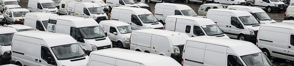 Rows upon rows of white Ford Transit Vans parked in a large compound, showcasing the scale of Britain’s most popular commercial vehicle and its dominance on UK roads for 60 years.