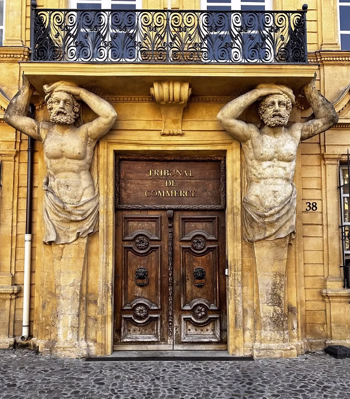 Golden Stone Architecture – An ornate yellow stone building in France with two carved male statues supporting the doorway, inspiring warm golden and earthy tones.