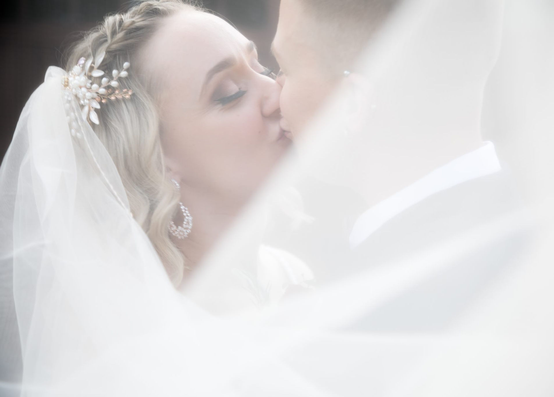 Two brides kiss on their wedding day behind a veil of softness