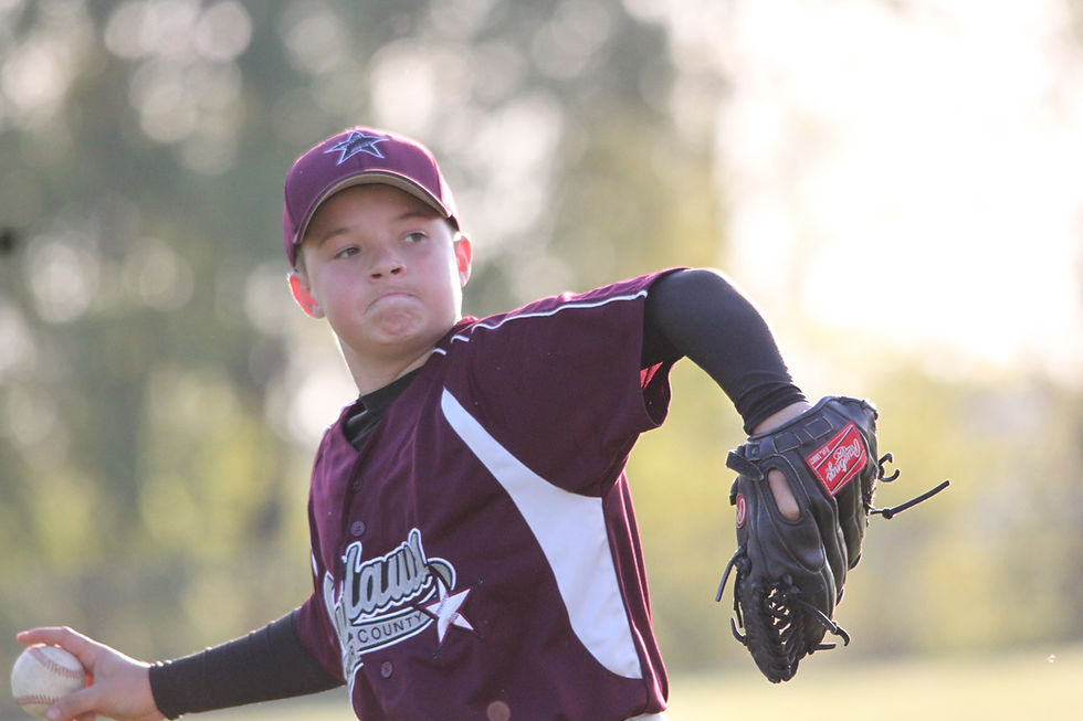 Young baseball pitcher in maroon uniform throws a ball on a sunny field, focused, with a glove and team logo.