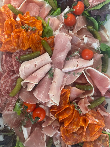 Charcuterie platter with prosciutto, salami, chorizo, cherry tomatoes, and cornichons on a bed of fresh greens.