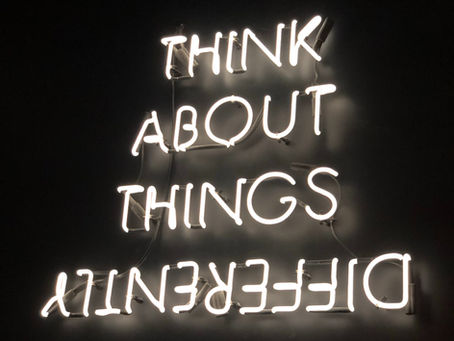 Upside down neon sign with the motivational quote Think About Things Differently glowing in white on a dark background