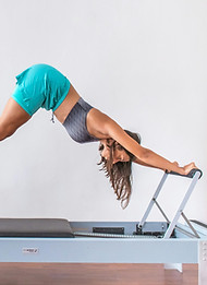 Mulher com calções verdes a fazer Pilates numa reformer. aparelho de pilates
