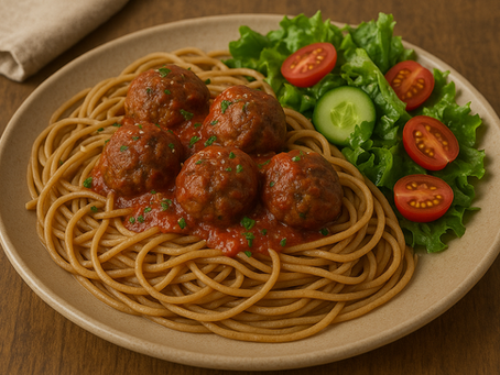 Plate of whole-grain pasta topped with beef and pork meatballs in tomato sauce, served with a side salad of greens and cherry tomatoes.