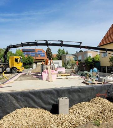 gelber LKW der mit ausgefahrenem Kran und einer Schaufel, Erde auf einer Baustelle ablädt