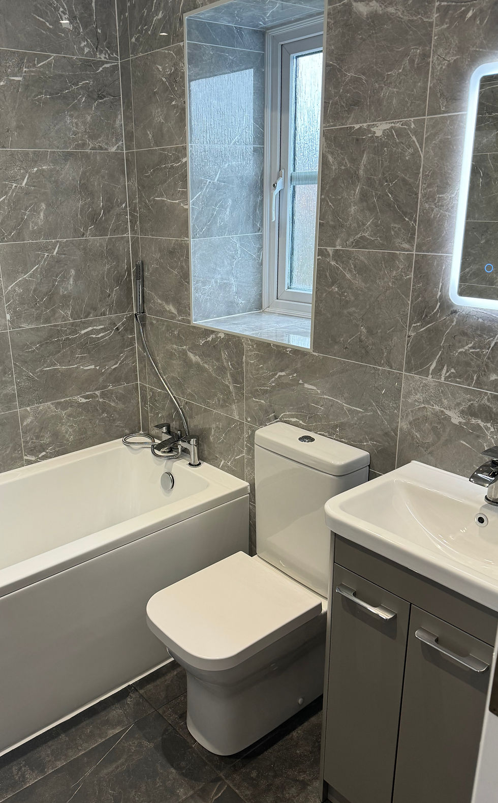 Main bathroom with bath, toilet and grey tiles