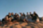 Group of friends sitting on patterned blankets atop a sand dune, enjoying the last light of the day.