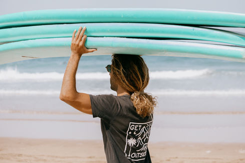 A surfer carrying a stack of surfboards on the beach in Mirleft, Morocco.