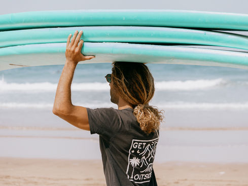 A surfer carrying a stack of surfboards on the beach in Mirleft, Morocco.