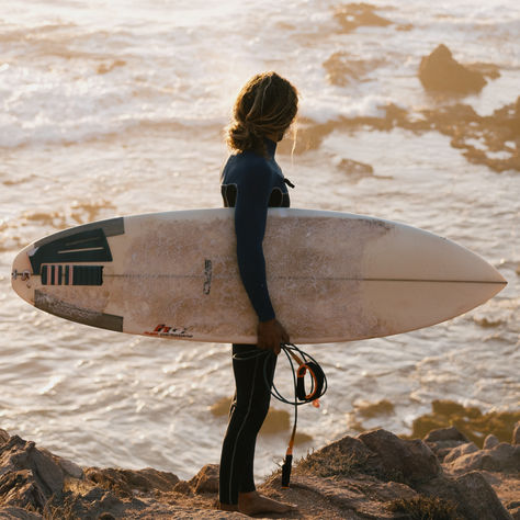 Surfer holding a board and looking at the ocean during golden hour in Mirleft, Morocco