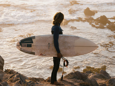 Surfer holding a board and looking at the ocean during golden hour in Mirleft, Morocco