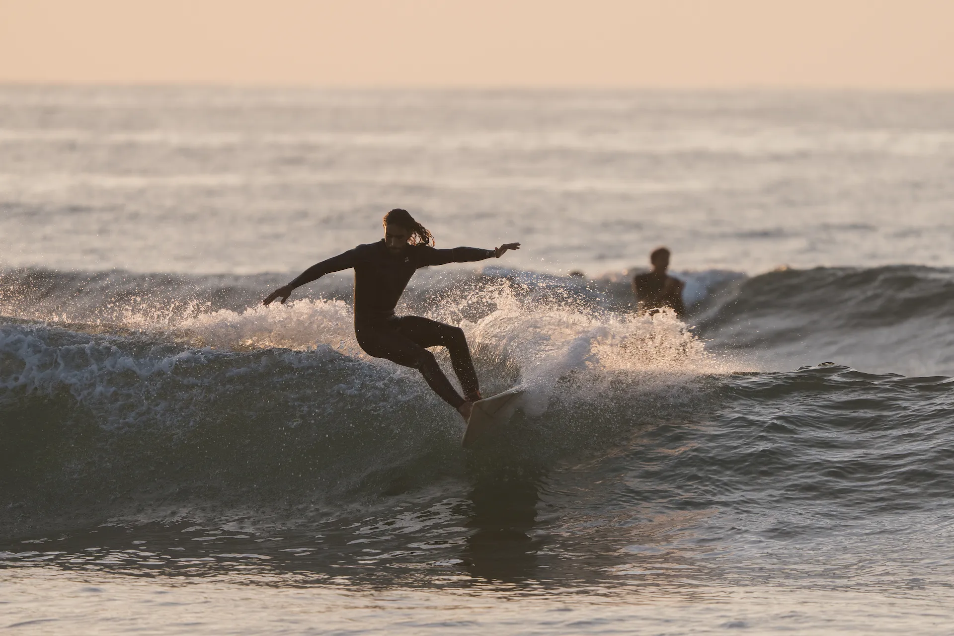 Surfer riding a wave at sunset, demonstrating the balance and control developed through surf trainin