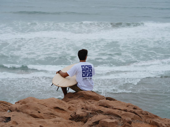 Surfer sitting above the ocean in Mirleft, reflecting before a surf session