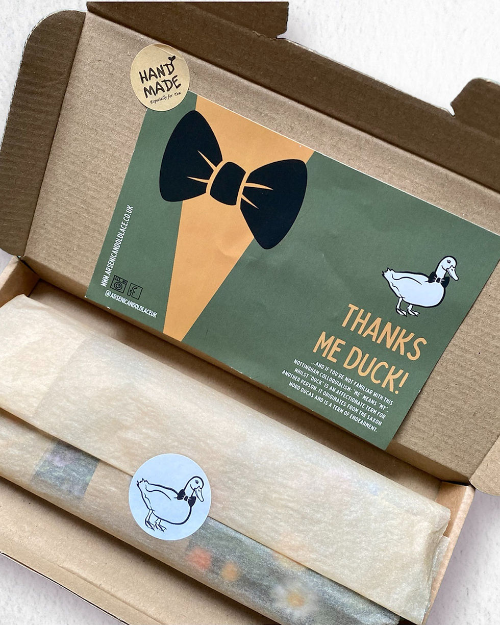 Open cardboard box with a green and orange card reading "THANKS ME DUCK!" featuring a bowtie and duck illustration. Handmade label attached.