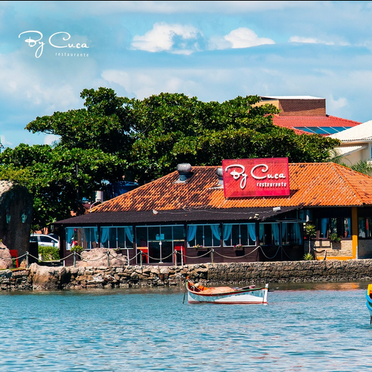 Imagem do restaurante em luz do dia, com o mar e um barco de pequeno porte