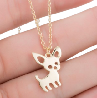 Close-up of a gold-tone Fidèle Chihuahua dog necklace displayed on fingers
