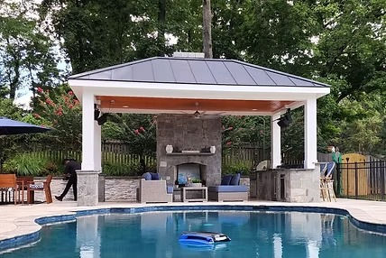 Covered patio with stone fireplace, lounge seating, and outdoor kitchen by NOVA Landscape Construction
