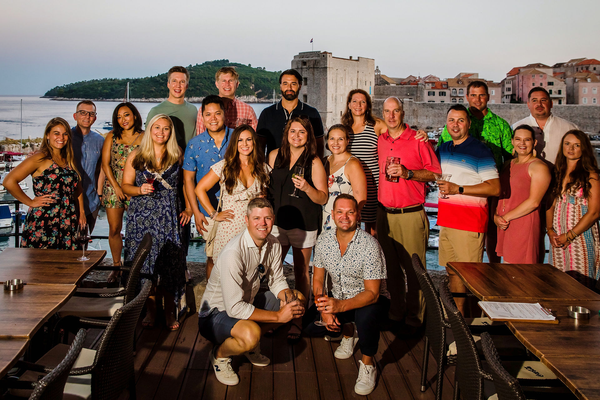 A smaller group of travelers dressed for dinner gather for a sunset photo on a restaurant deck overlooking the Dubrovnik harbor.