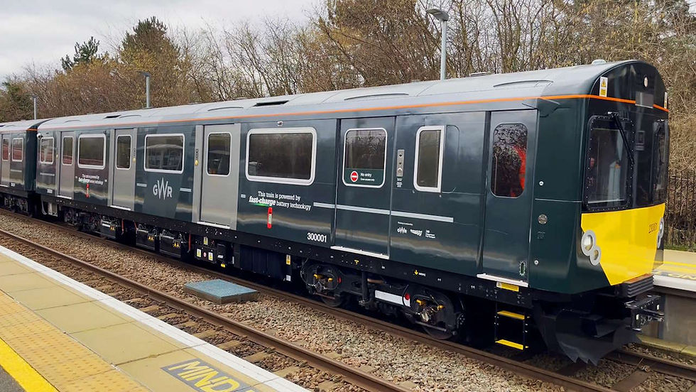 Battery-powered train in dark green and yellow at a station, with trees in the background. Text on train: "This train is powered by fast-charge battery technology.”