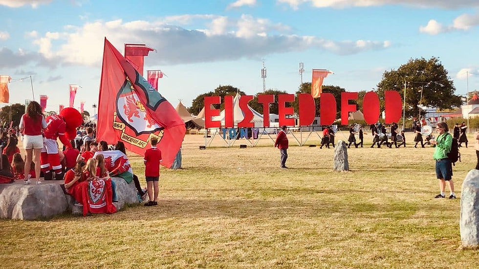 Eisteddfod sign in an open field with people waving Wrexham flag.