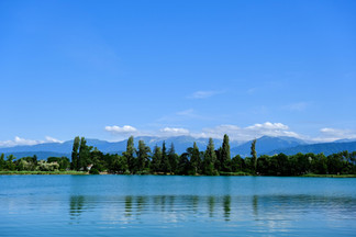 Reflection of tress on lake with mountains in the background and a blue sky.