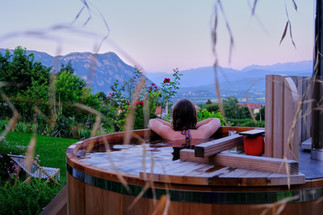 Woman sits in wooden hot tub looking out to view of the mountains and roses.